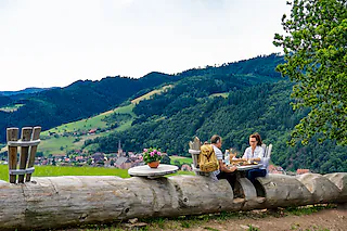 Die lange Baumstamm-Bank am Schwarzwälder Genießerpfad „Harmersbacher Vesperweg“ in Oberharmersbach. Im „Donissi Hofladen“ von Markus Schwarz lässt sich der Rucksack mit regionalen Spezialitäten füllen – fürs Picknick auf der Tour. [Foto: Tourist-Information Oberharmersbach.jpg]